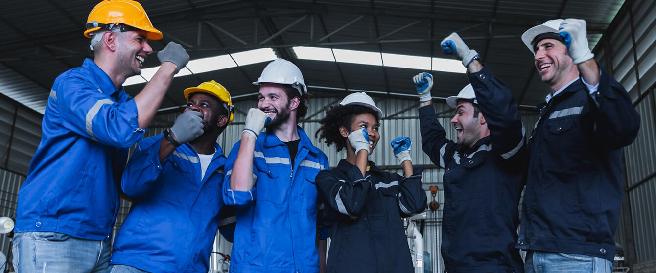 Fünf Elektriker in Arbeitskleidung feiern Teamgeist in Industriehalle