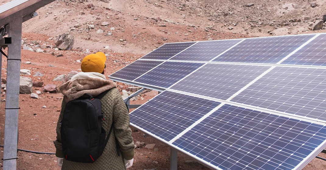 Person mit Rucksack inspiziert Solarmodule auf Freiflächenanlage