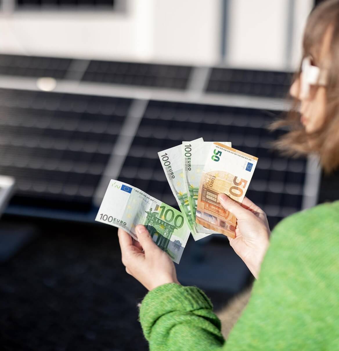 Frau hält Euro-Scheine vor Solarmodulen auf Hausdach — Nahaufnahme