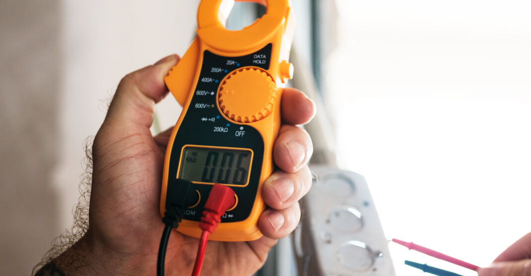 Hand hält digitales Zangenamperemeter für Elektromessung bei Steckdose