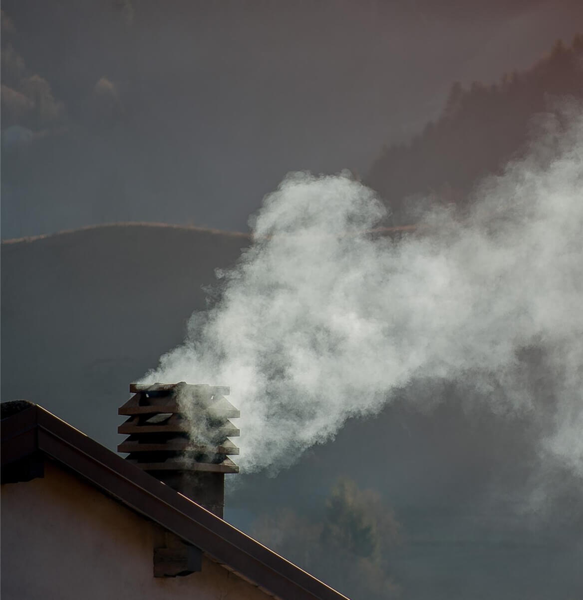 Rauch steigt aus Schornstein eines Hauses auf dunklem Wolkenhimmel