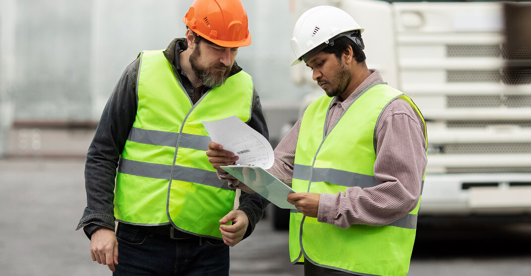 Zwei Elektriker mit Schutzhelmen besprechen Baupläne auf Baustelle