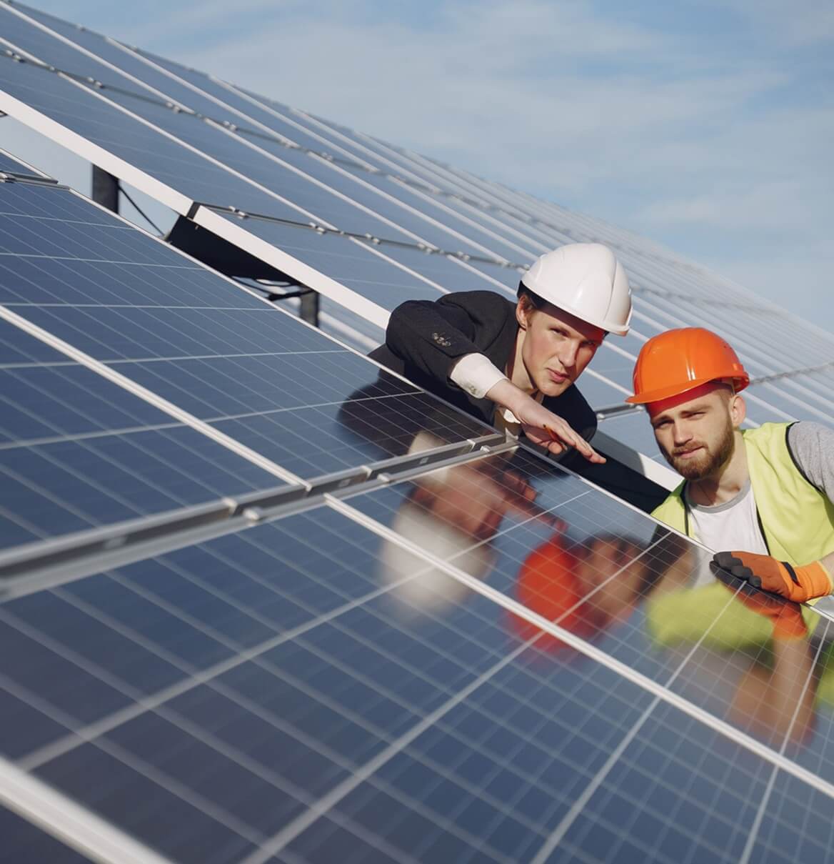 Zwei Techniker mit Schutzhelmen untersuchen Photovoltaikmodul aus der Nähe