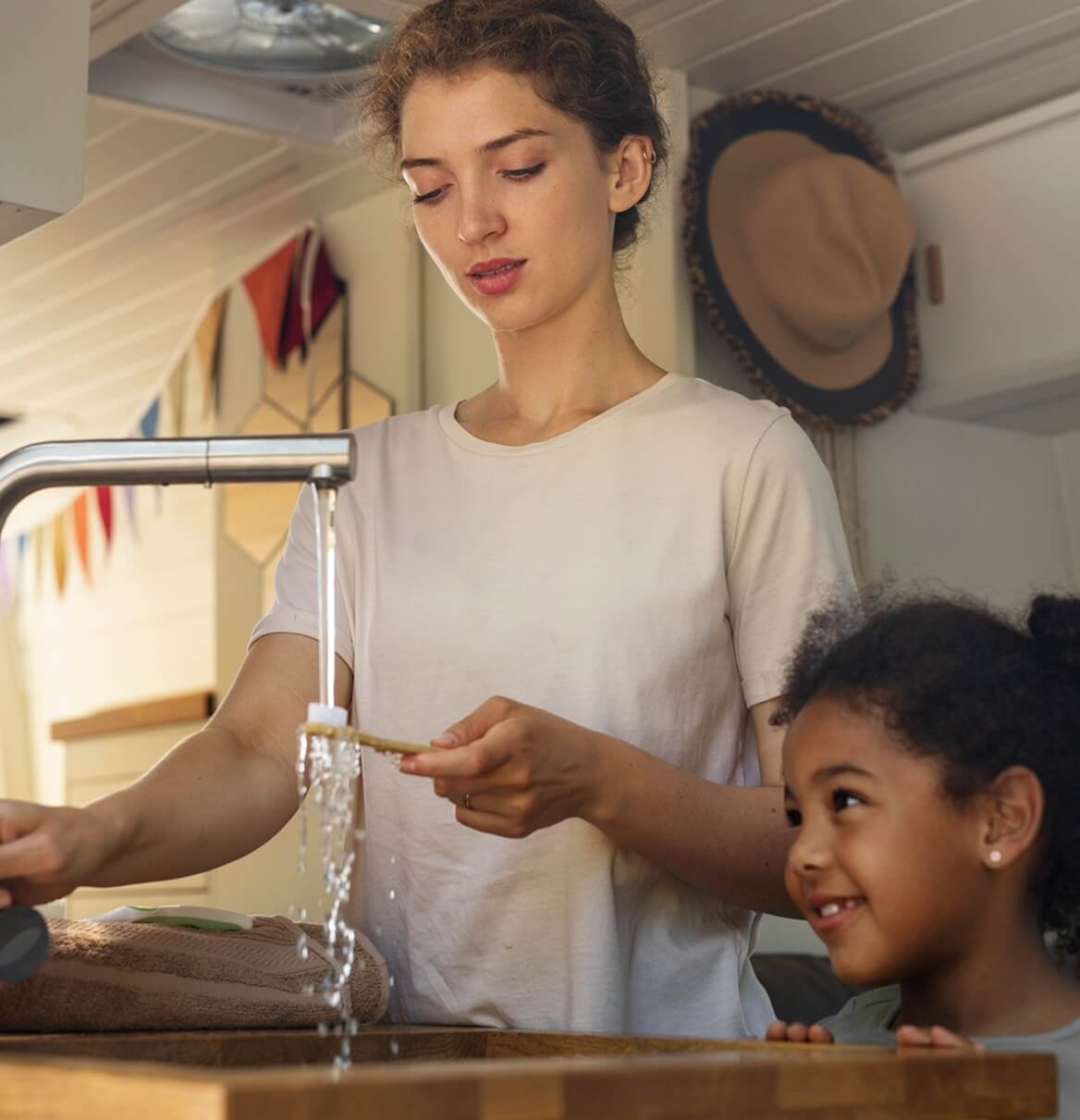 Mutter und Kind am Küchenwasserhahn als Symbol für Energieeffizienz im Haushalt