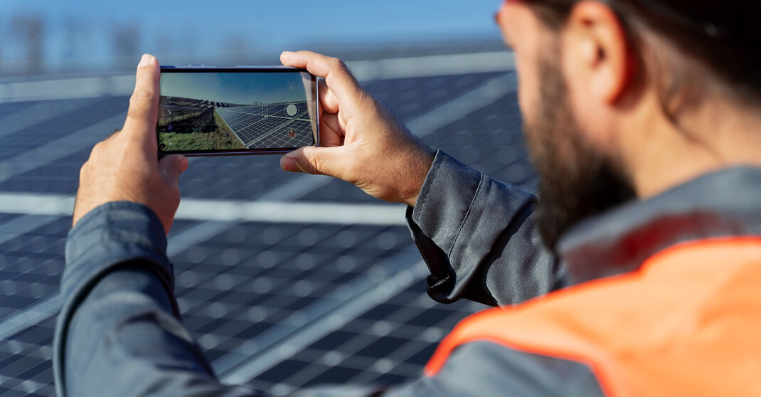 Techniker in Warnweste fotografiert Solarmodule zur Dokumentation mit Smartphone