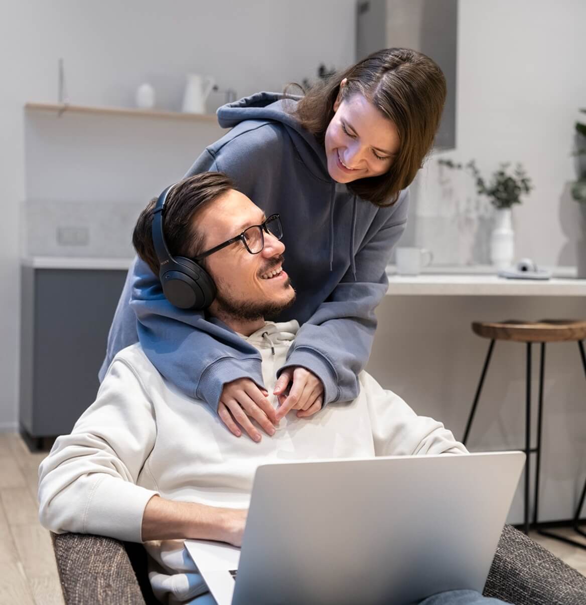 Paar sitzt im modernen Wohnzimmer mit Laptop und Kopfhörern bei Nacht